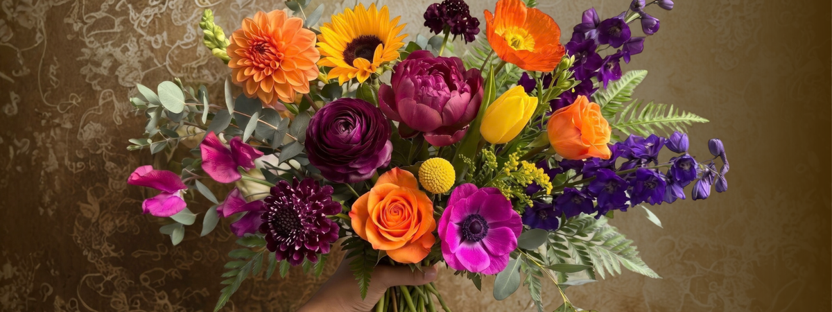 Colorful best friend flower bouquet with vibrant roses, sunflowers, and purple and pink blooms against a decorative background.