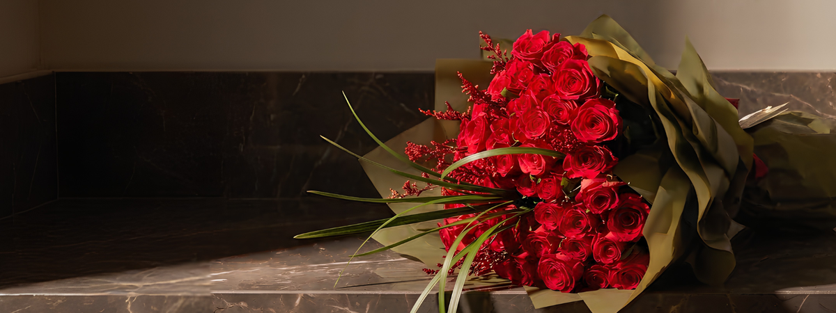Red rose bouquet wrapped in elegant golden-brown paper, perfect for a romantic anniversary flower gift.