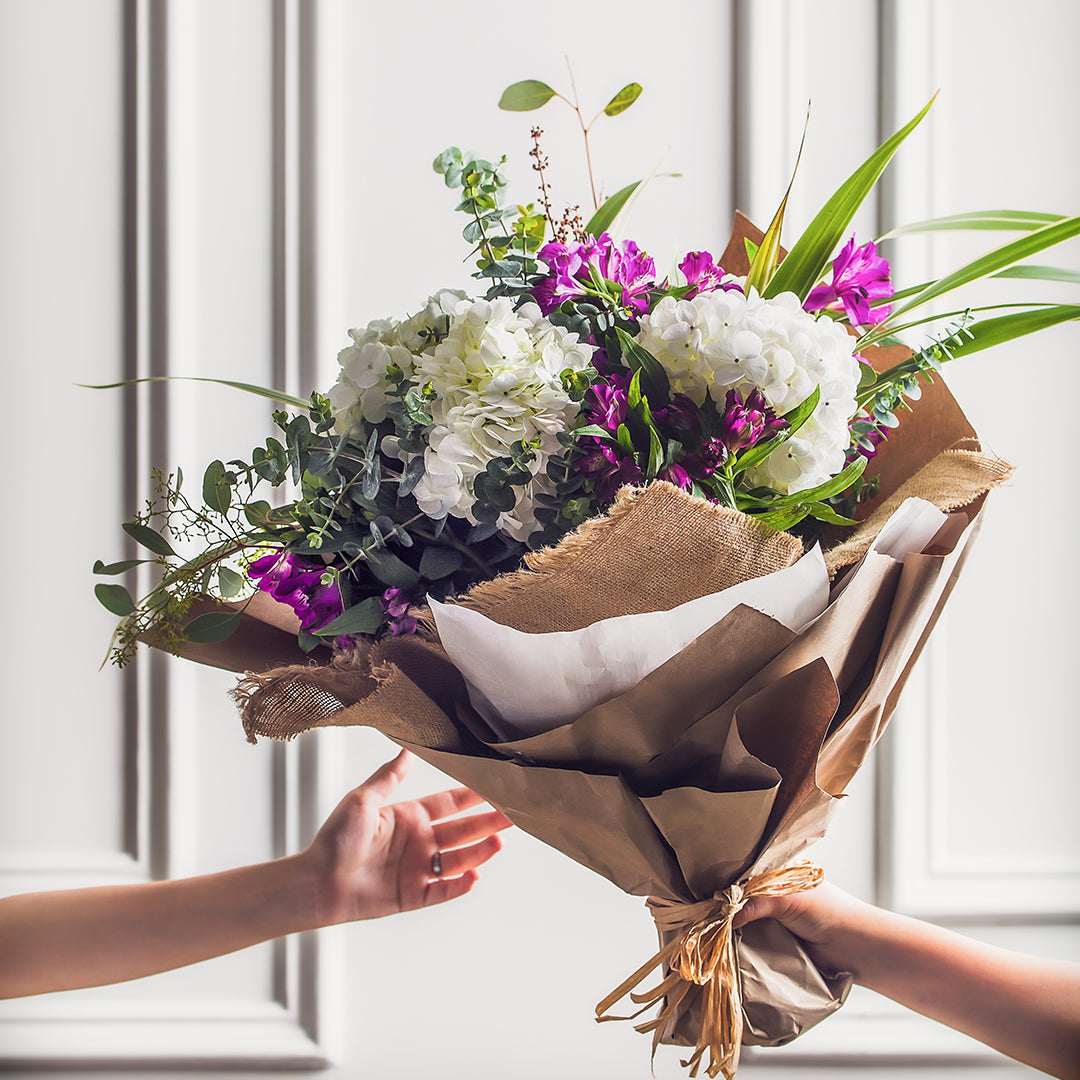 Hands gifting a large flower bouquet to a recipient for a special occasion.